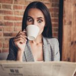 WOW! Close up portrait of astonishment brunette woman with crazy emotion and stare open eyed read the news about high oil prices drink espresso beverage from a white small mug in loft workstation